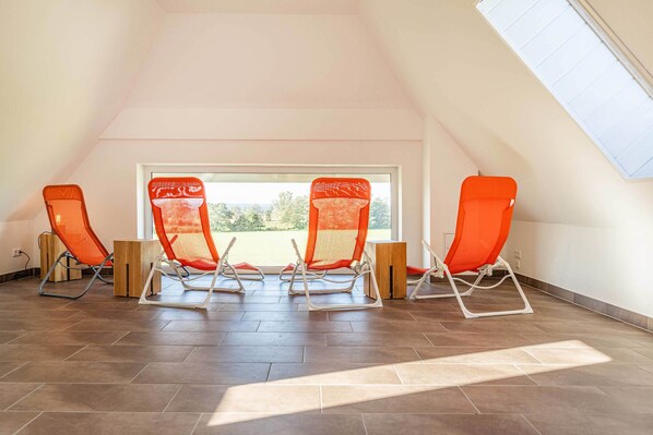 A room with three orange lounge chairs, a large window, and a sloped ceiling. - Charming vacation apartment for two with sauna & relaxation room (Loddin)