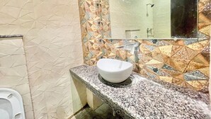A bathroom with a white sink, patterned tiles, and a mirror reflecting a shower area.