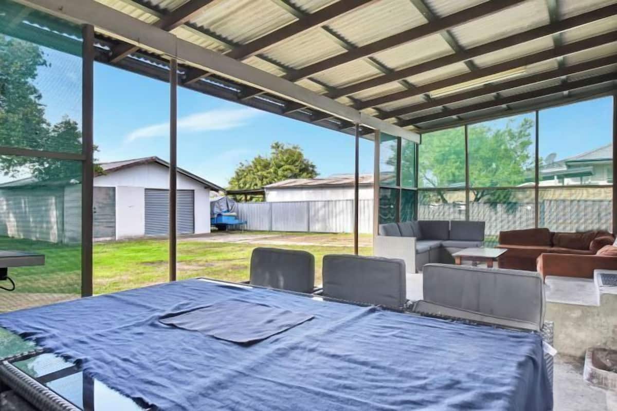 Un espace extérieur abrité, équipé d’une table et de chaises, d’un lit à baldaquin et offrant une vue sur le jardin arrière.