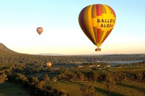 En luftballon med teksten 'Balloon Aloff' på, svæver over et landskab med træer og et vandareal.