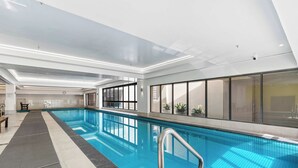 Ein Hallenbad mit klarem, blauem Wasser, gefliestem Boden und einer Metallleiter.