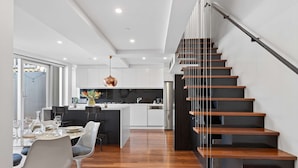 A modern kitchen with white cabinets, a dining area with a round table and chairs, and a wooden staircase. - City Escape - Split Level City Loft & Balcony (Sydney)
