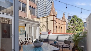 An outdoor patio with a table, chairs, potted plants, and a view of a historic building. - City Escape - Split Level City Loft & Balcony (Sydney)