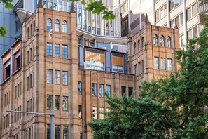 Ein mehrstöckiges Gebäude mit Hauseingang an der Ecke, großen Fenstern und einem sichtbaren Balkon.