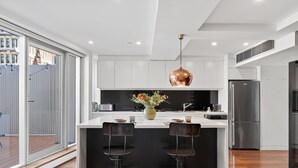A modern kitchen with a central island, bar stools, a hanging pendant light, and a stainless steel refrigerator. - City Escape - Split Level City Loft & Balcony (Sydney)