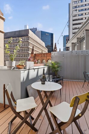 Eine Dachterrasse mit Tisch und Stühlen, Blumentöpfen und Blick auf die Stadtgebäude.