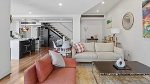 A modern living room with a sofa, a coffee table, and a dining area with chairs and a table. - City Escape - Split Level City Loft & Balcony (Sydney)