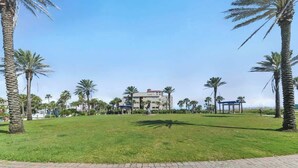 A grassy area with palm trees, a building with a statue, and a paved walkway. - 3 Blocks to Beach: Beachside Escape Coastal Oasis (Jacksonville Beach)
