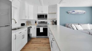 A modern kitchen with white cabinetry, stainless steel appliances, and a wooden floor. - 3 Blocks to Beach: Beachside Escape Coastal Oasis (Jacksonville Beach)