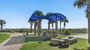 A park with a curved blue canopy structure, palm trees, and a paved walkway. - 3 Blocks to Beach: Beachside Escape Coastal Oasis (Jacksonville Beach)