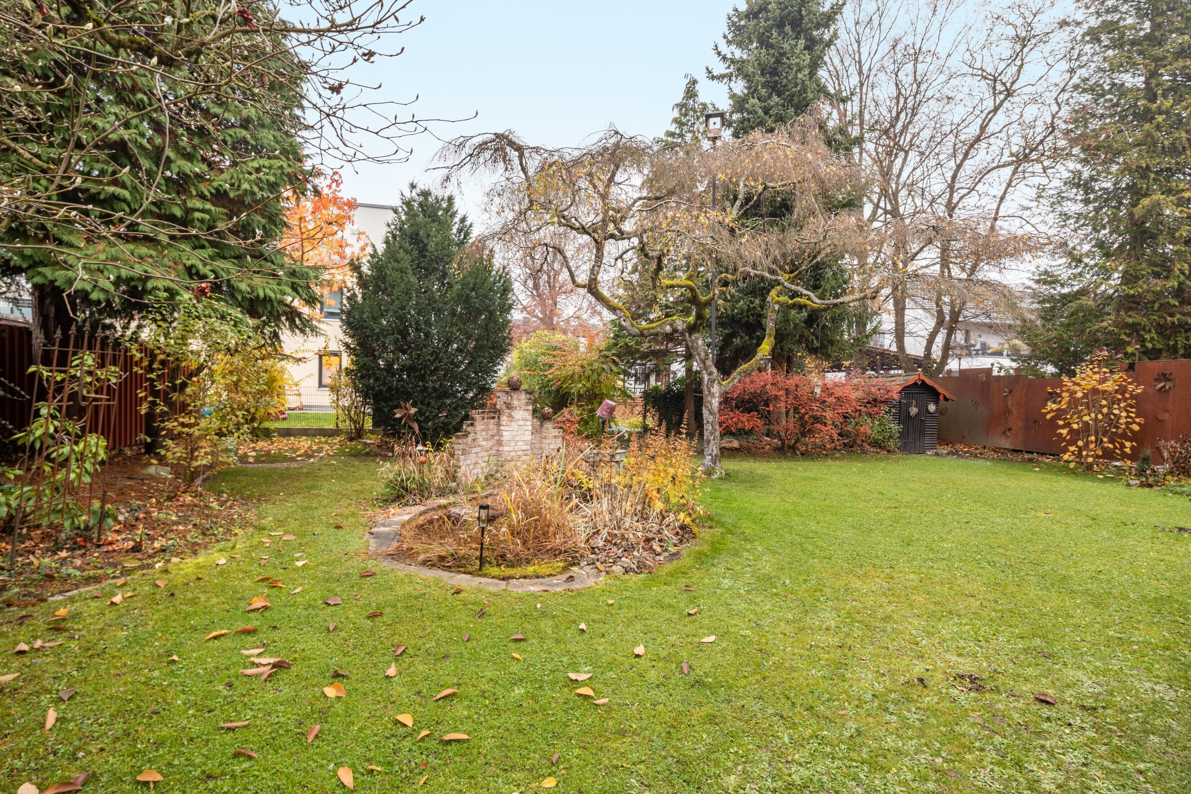 A garden with a lawn, trees, and a brick structure.