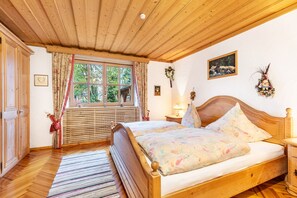 Camera da letto con struttura in legno, un letto, una finestra con tende, un comodino con una lampada e un quadro appeso al muro.
