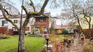 Un jardin agrémenté d’une structure en pierre, d’une clôture en bois et, au fond, d’un bâtiment doté d’un balcon.