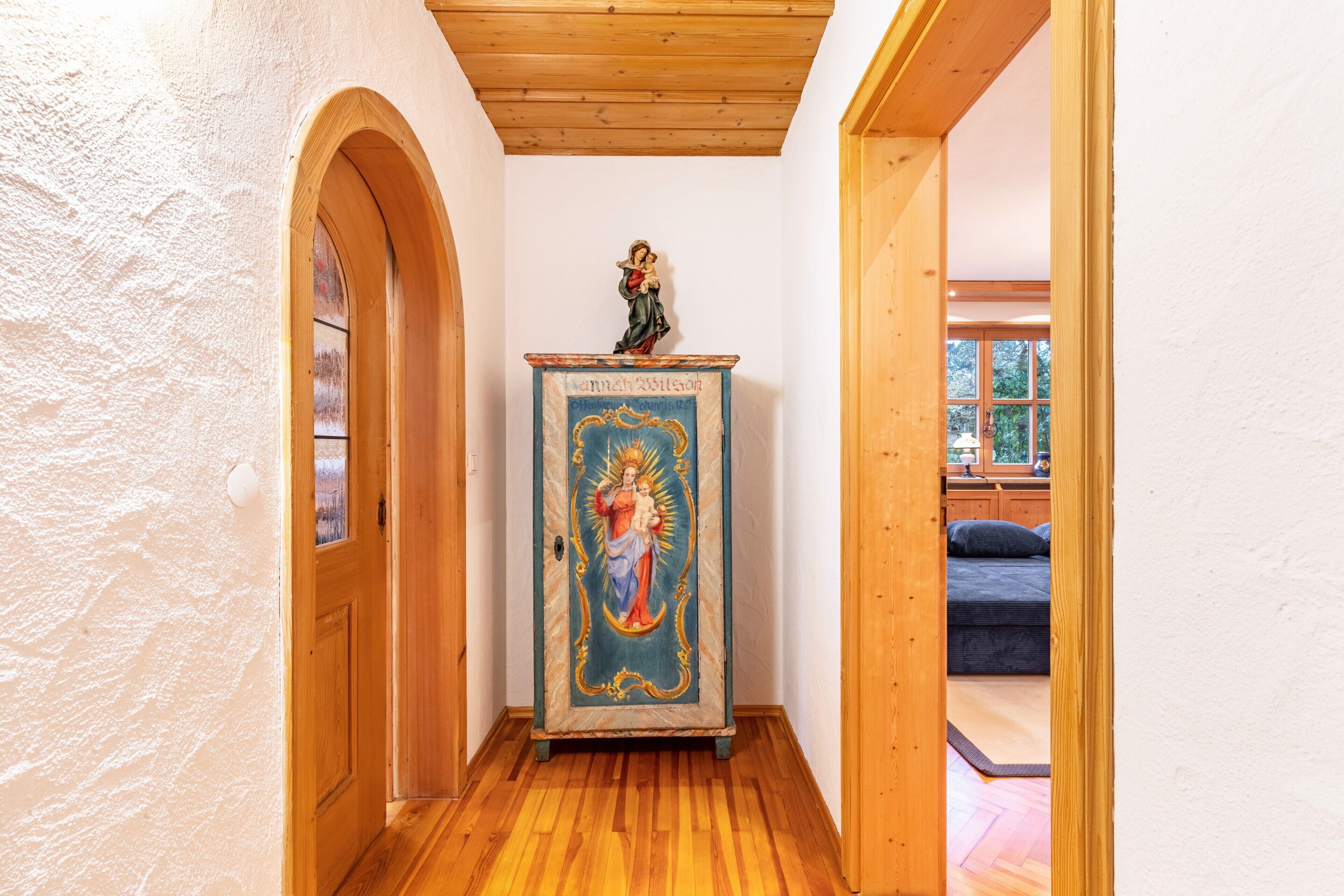 A narrow hallway with wooden flooring and a statue on a pedestal.