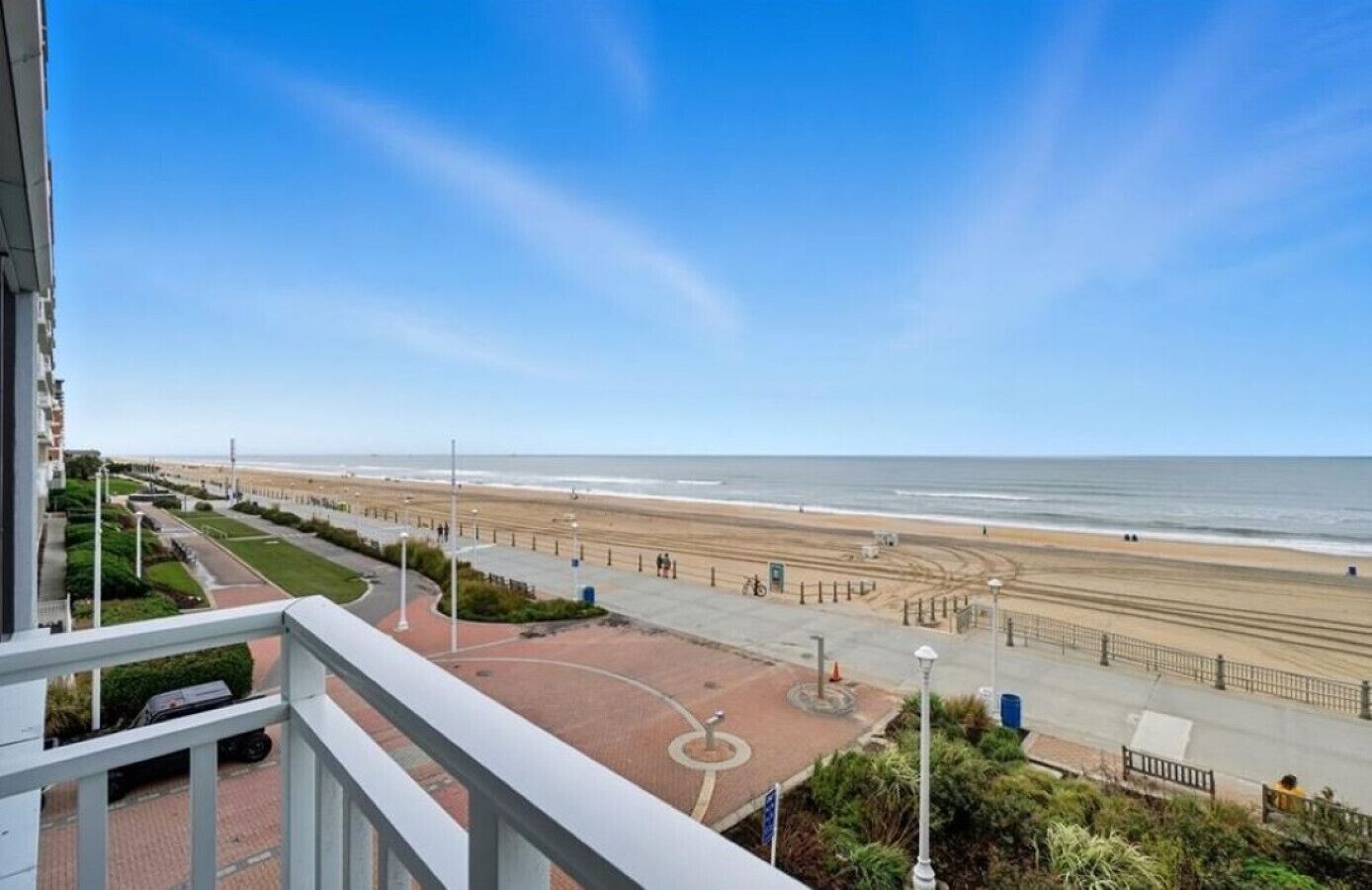 Vista al mar desde un balcón, con un paseo pavimentado, la playa y el océano.