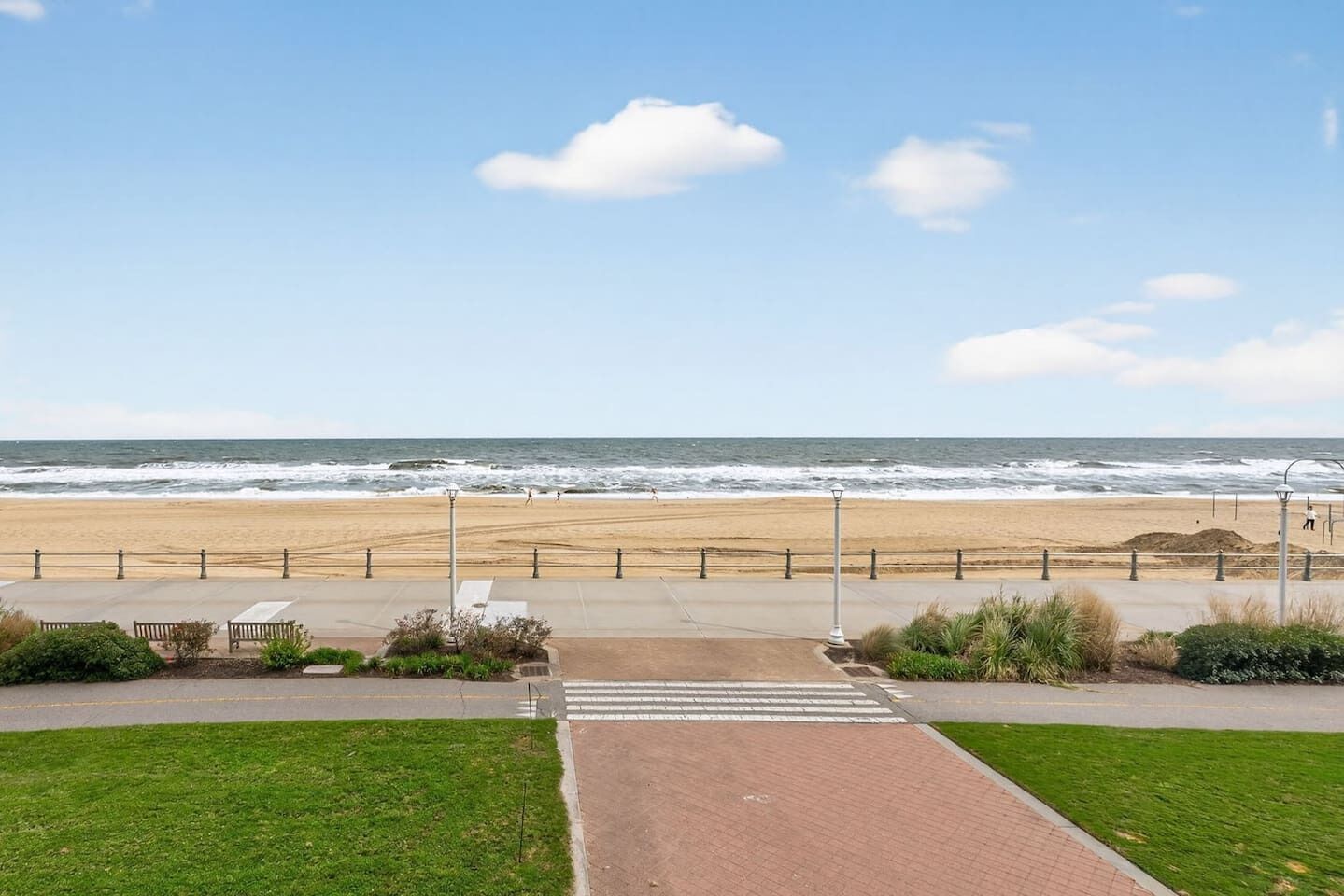 A coastal walkway leading to a beach with a clear view of the ocean.
