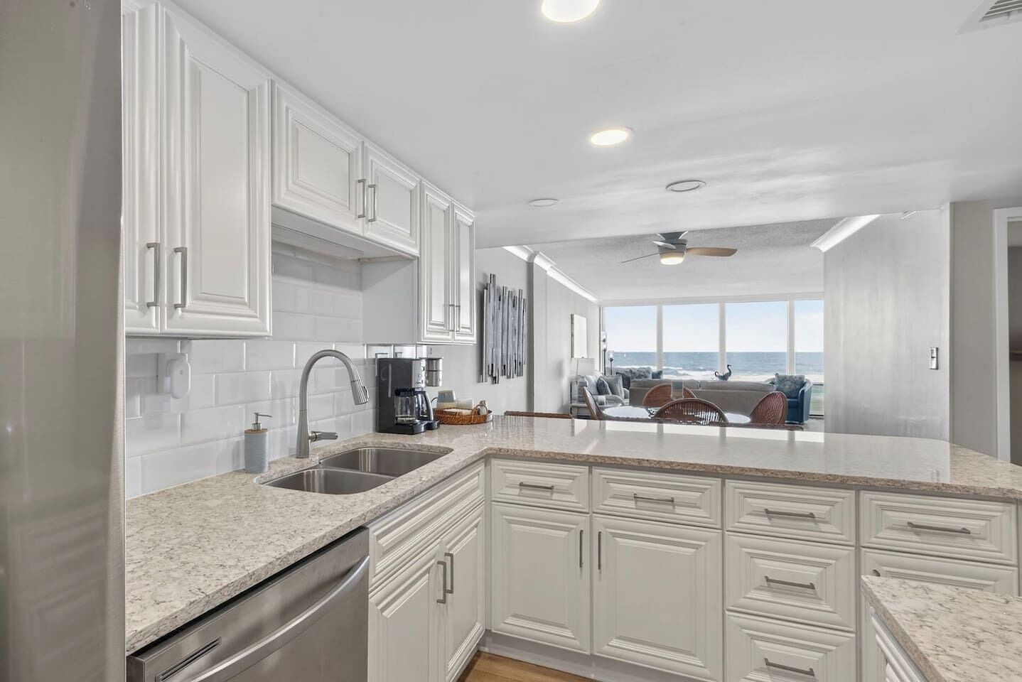 A modern kitchen with white cabinetry, granite countertops, and a view of the ocean through large windows.
