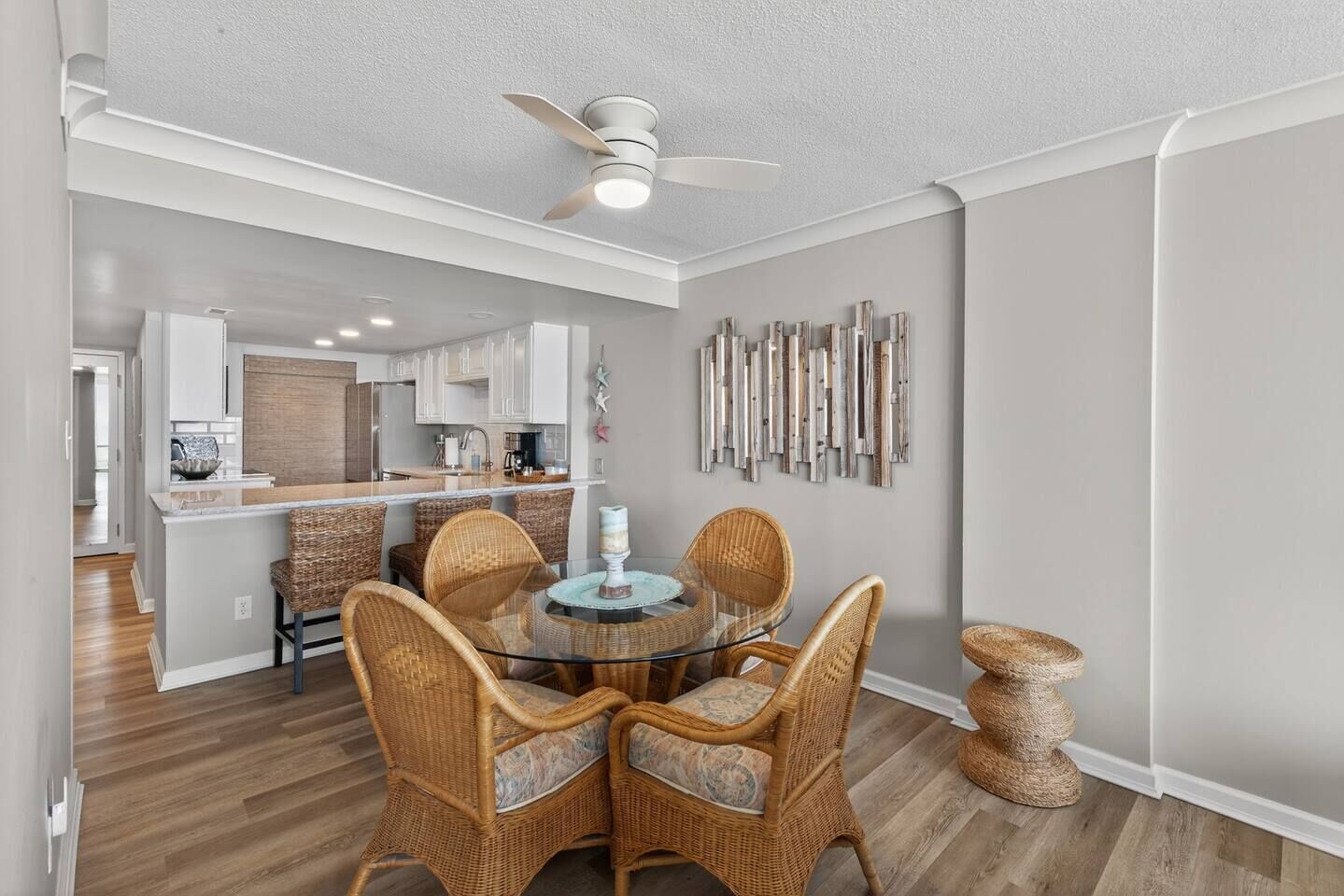 A modern kitchen with white cabinets, a dining area with wicker chairs and a glass table, and a ceiling fan.