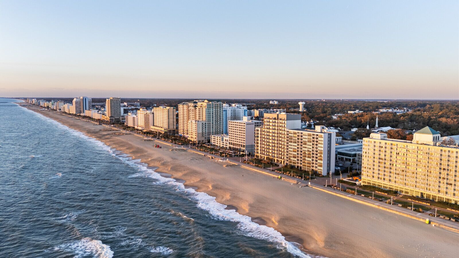 A coastal cityscape with a beachfront hotel featuring multiple high-rise buildings, a sandy beach, and a clear sky.