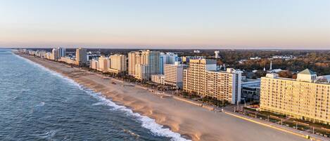 A coastal cityscape with a beachfront hotel featuring multiple high-rise buildings, a sandy beach, and a clear sky.