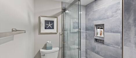 A modern bathroom with a glass shower enclosure, a toilet, and a framed starfish decoration.