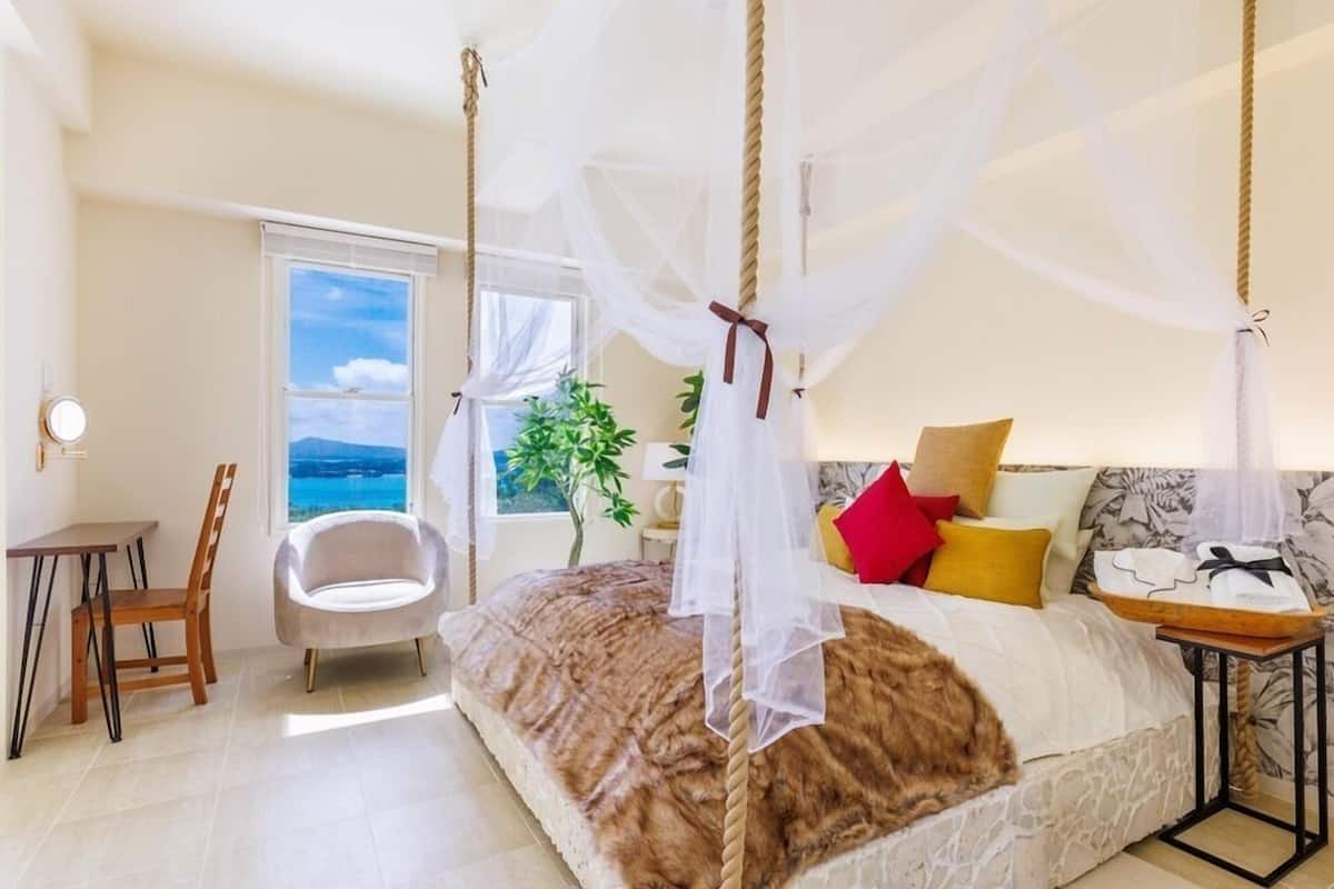 Een slaapkamer met een bed, een stoel, een tafel en uitzicht op zee.