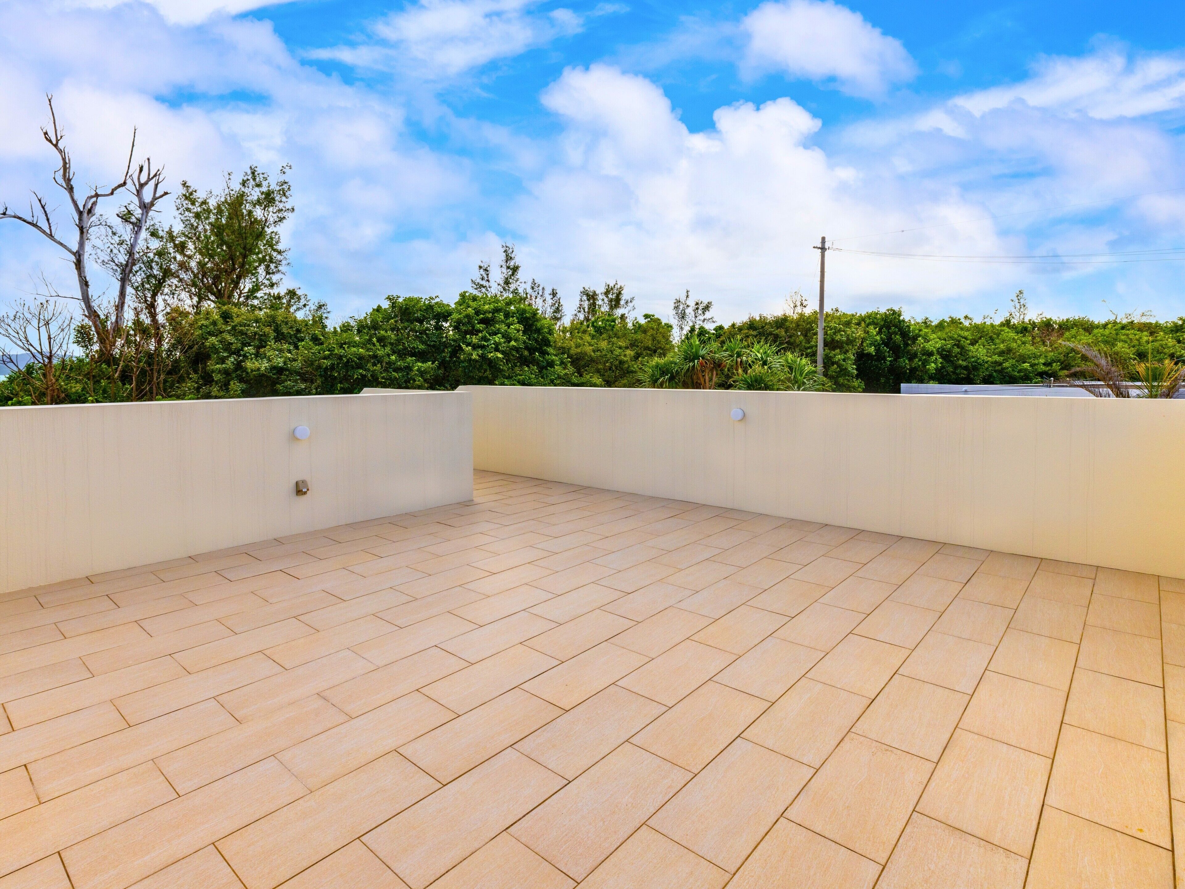Une terrasse sur le toit, dotée d’un sol carrelé, entourée d’un mur blanc et de verdure.