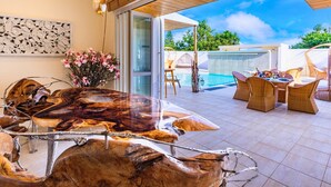 A modern outdoor dining area with a glass-top table, wicker chairs, and a pool in the background. - Resort Villa KAPUKA KOURIJIMA (Nakijin)