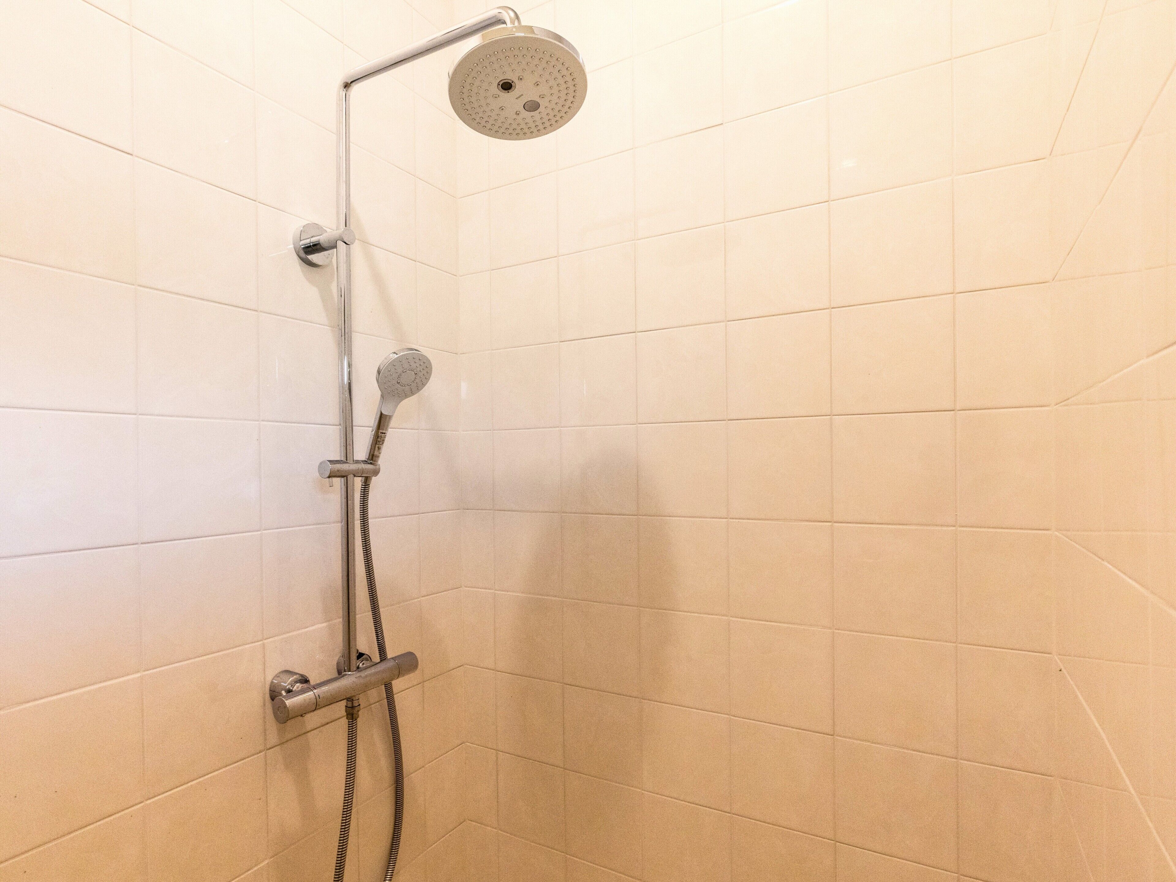 Suihkussa on sekä käsisuihkupää että ylhäältä asennettu suihkupää, ja molemmat on kiinnitetty seinään. Lattiassa on laatat.