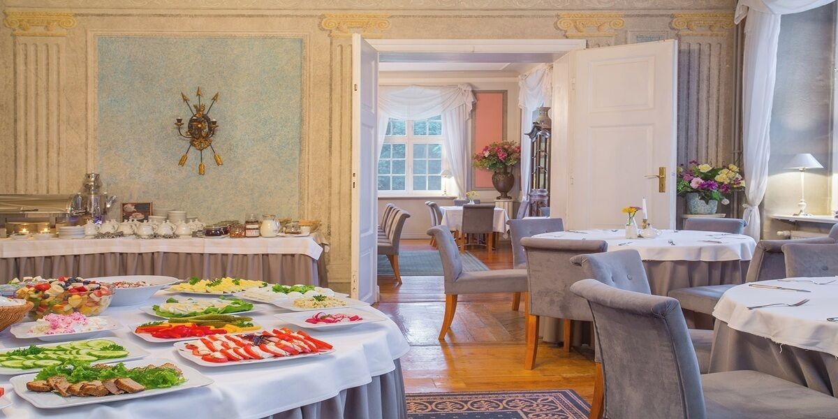 A dining area with multiple tables set for a meal, featuring a variety of dishes and a chandelier.