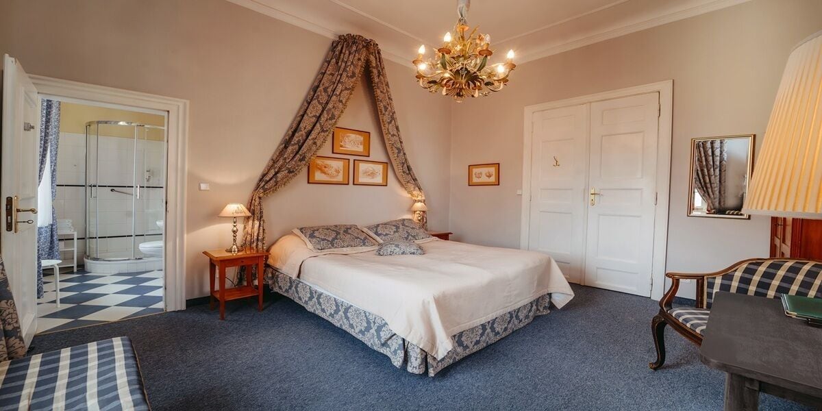 A bedroom with a bed, a chandelier, a bedside table, a chair, and a door.
