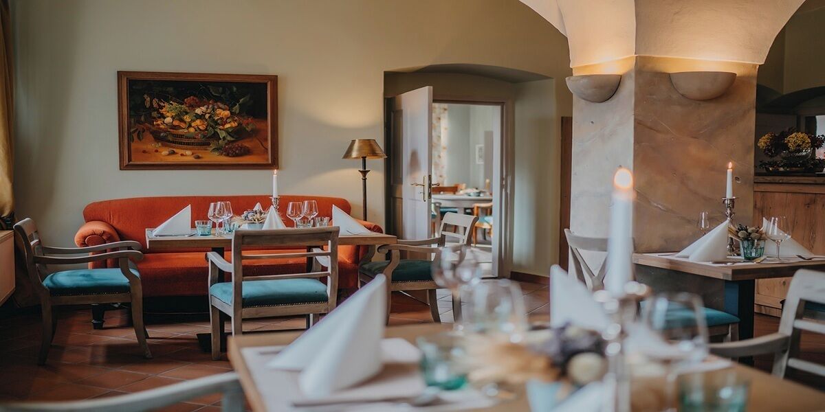 Un comedor con un sofá rojo, sillas de madera y una mesa preparada para una comida.