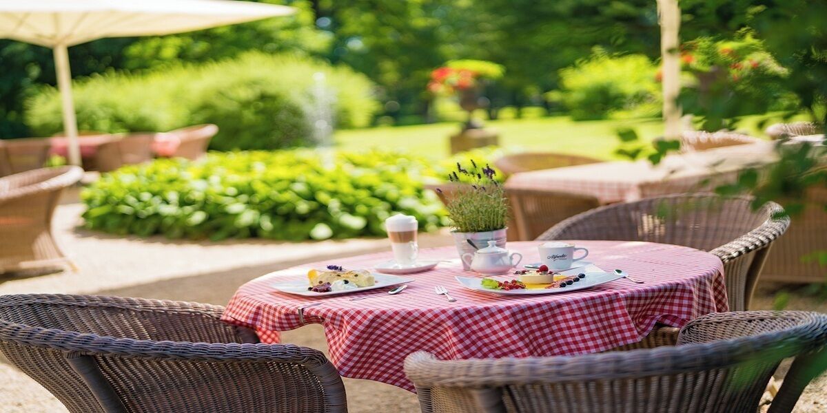 Un área de comedor al aire libre con sillas de mimbre y un mantel a cuadros rojo y blanco.