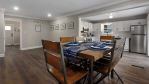 Un coin repas avec une table en bois dressée pour quatre personnes, une cuisine avec des meubles blancs et un réfrigérateur en acier inoxydable.