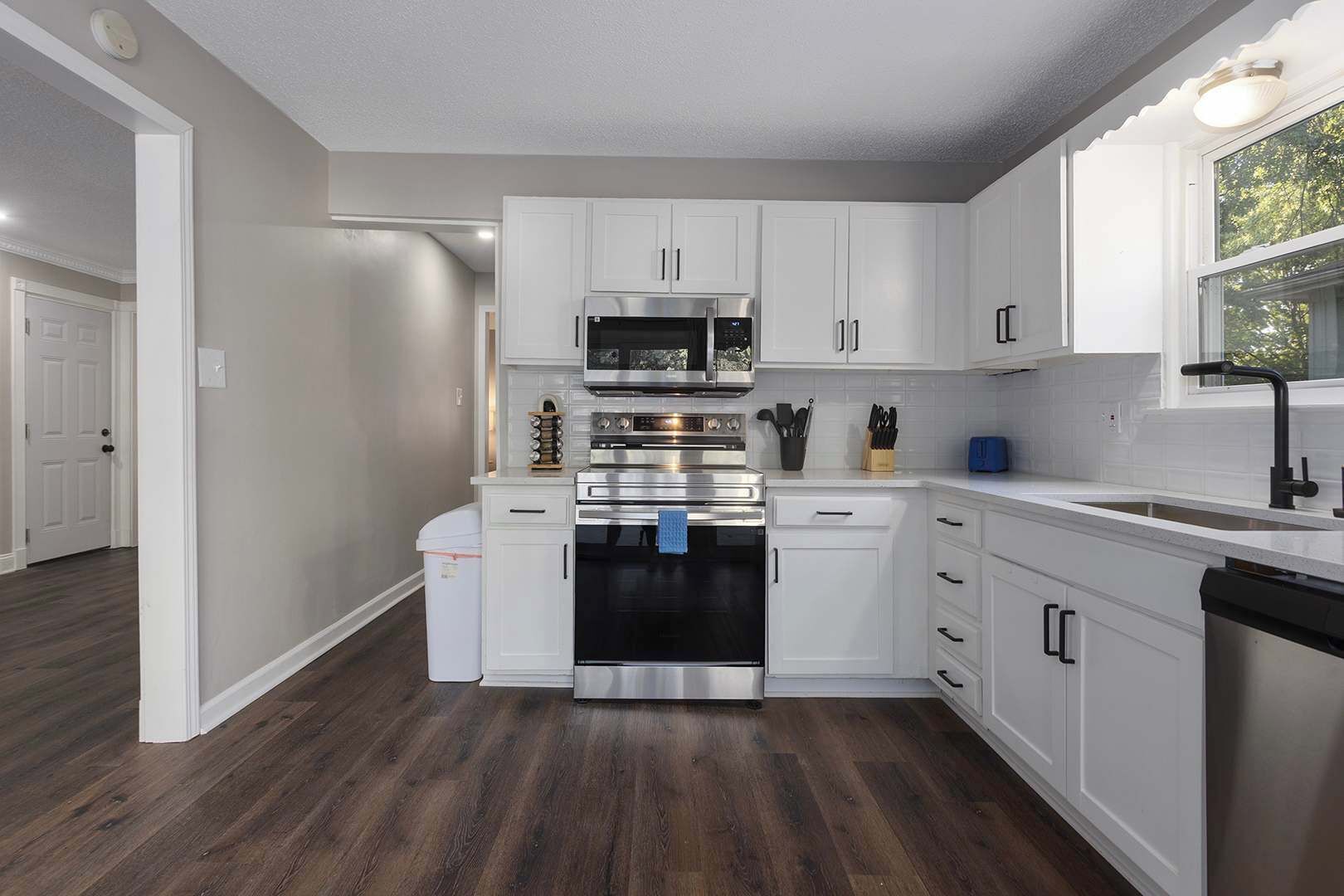 A modern kitchen with white cabinetry, stainless steel appliances, and a wooden floor.