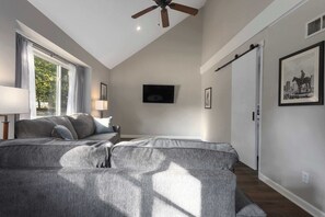 A room with a grey sofa, a ceiling fan, a TV mounted on the wall, and a framed picture on the wall.