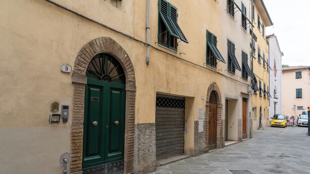 A street with a building featuring a green door, a stone archway, and a number '9' sign.