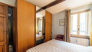 A bedroom with a bed, a wooden wardrobe, a chair, a radiator, and a window with curtains.