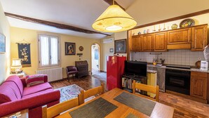 A cozy living room with a red sofa, wooden dining table, and a kitchen area with wooden cabinets and a red refrigerator.