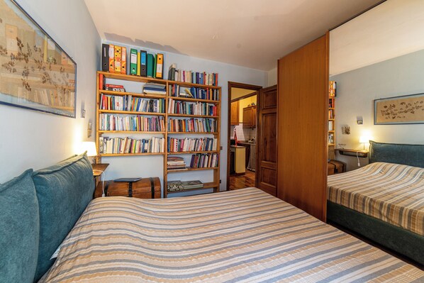 A bedroom with two beds, a bookshelf, and a painting on the wall.