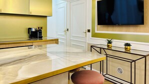 A modern kitchen with a marble countertop, gold cabinets, and a large flat-screen TV mounted on the wall. - Merveil Luxury Suite - Marais - Charlot (Paris)