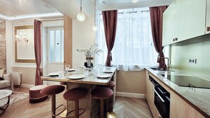 A modern kitchen with a dining area, featuring a central island with stools, a built-in oven, and a large window with curtains. - Merveil Luxury Suite - Marais - Charlot (Paris)