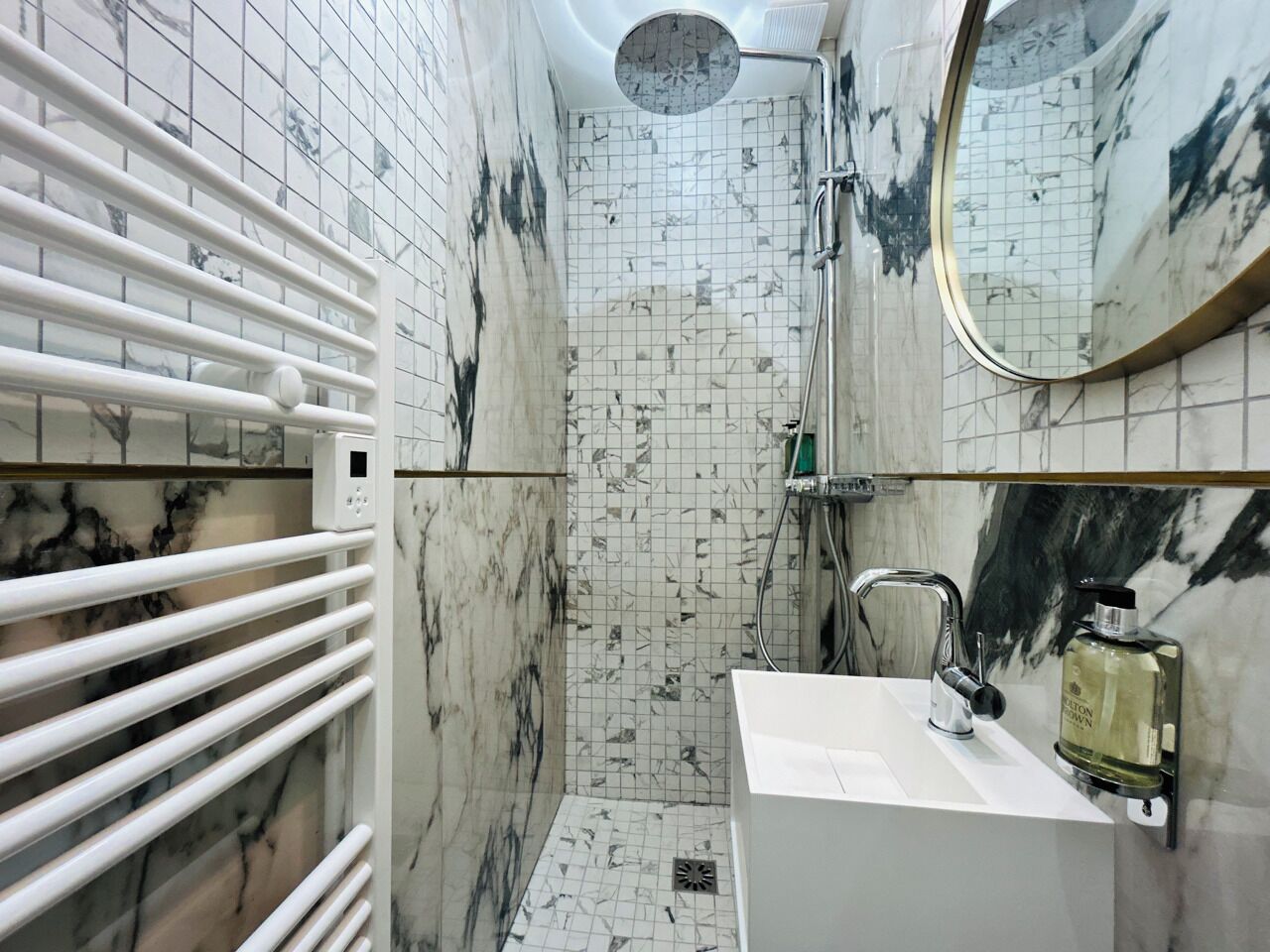 A bathroom with a white sink, a mirror, and a shower with a circular skylight.
