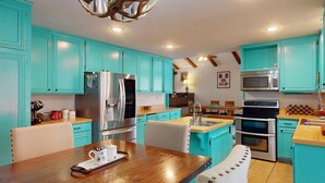 A kitchen with turquoise cabinets, stainless steel appliances, and a wooden dining table. - Pet Friendly | Monte Verde Lake | Fireplace | Deer Casa (Angel Fire)