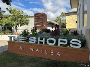 Schild für 'The Shops at Wailea' mit Holzkonstruktion und Grünpflanzen.