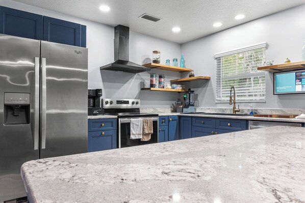A modern kitchen with stainless steel appliances, blue cabinets, and a marble countertop. - Spacious Mid-Century Modern Retreat near Spring (Crystal River)