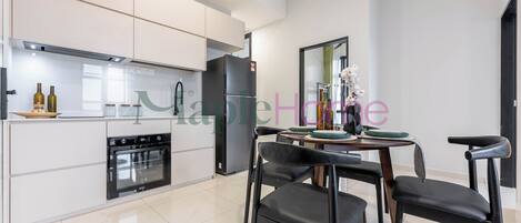 A modern kitchen with white cabinetry, a built-in oven, and a dining area with a round table and black chairs.