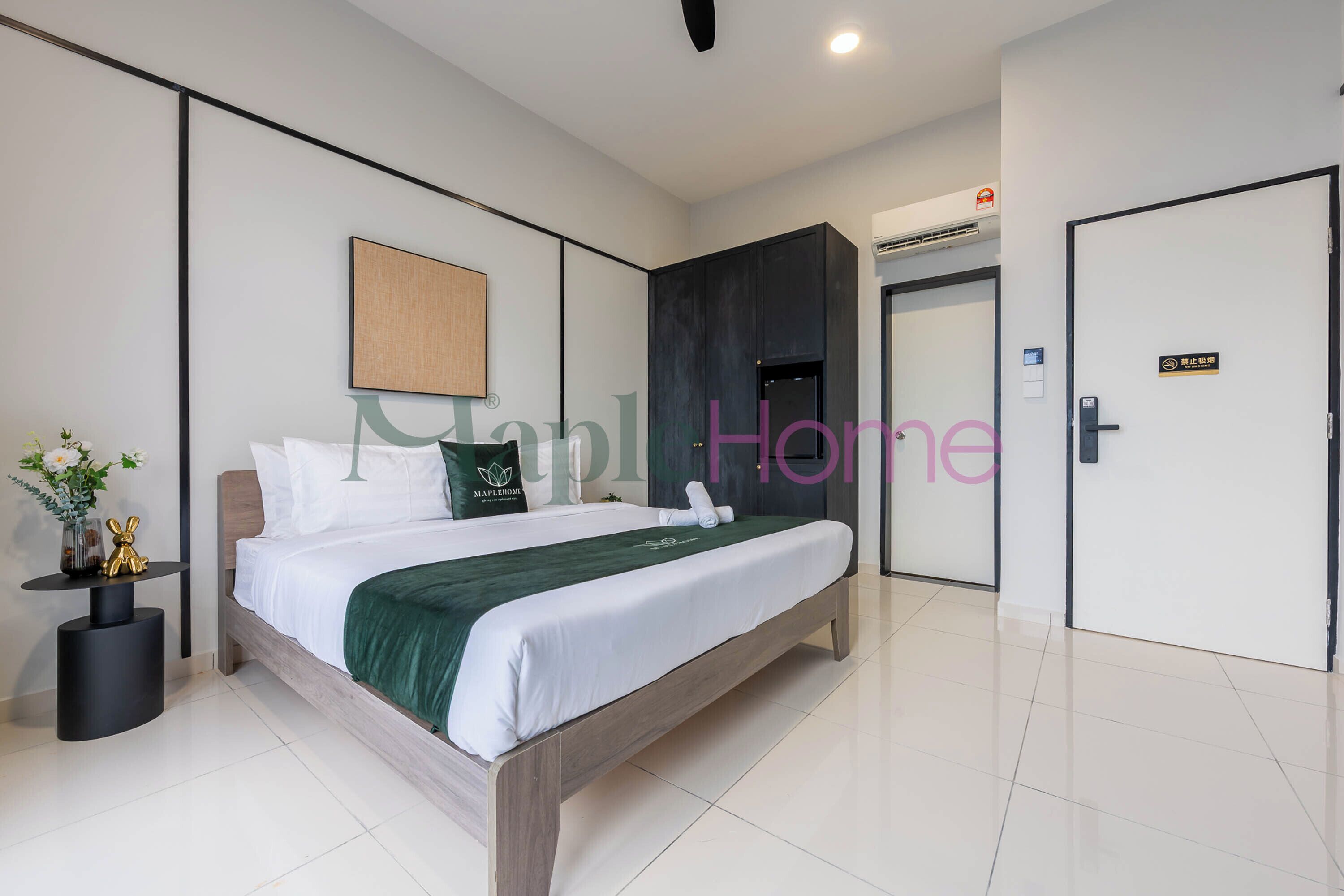 A modern hotel room with a large bed, a small side table with a vase, and a door with a sign.