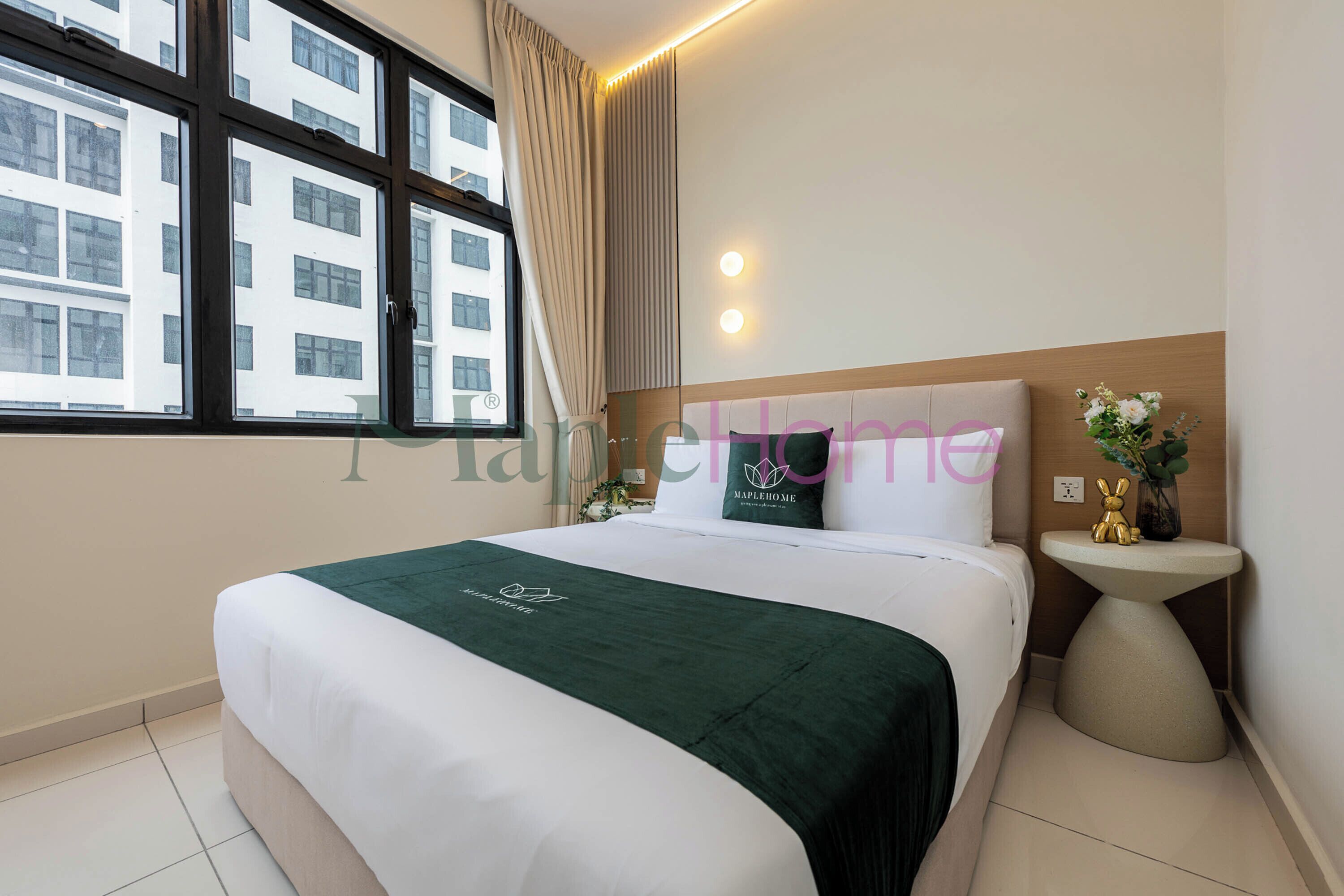 A hotel room with a large bed, a bedside table with a vase, and a window with curtains.
