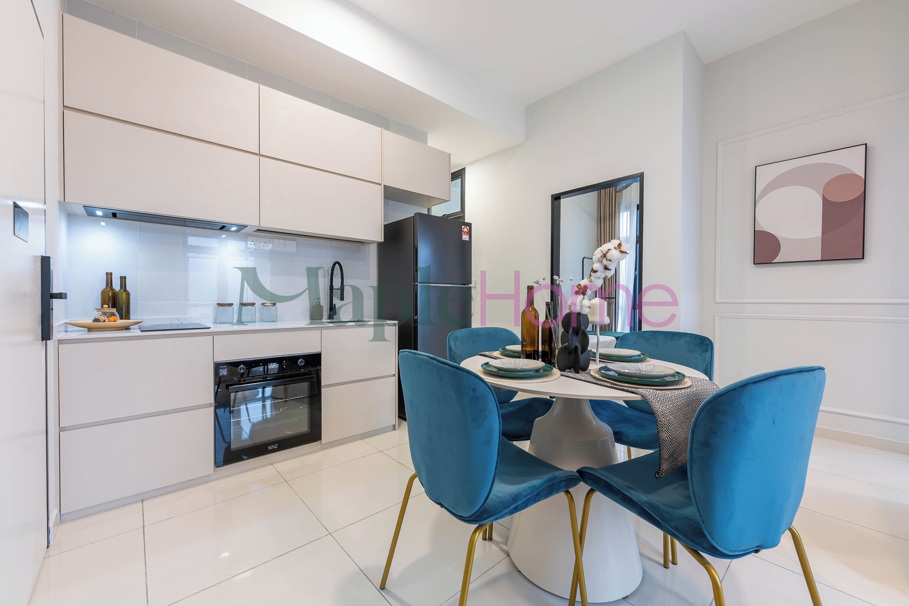 A modern kitchen with white cabinets, a black refrigerator, and a built-in oven. There is a dining area with blue chairs and a white table.